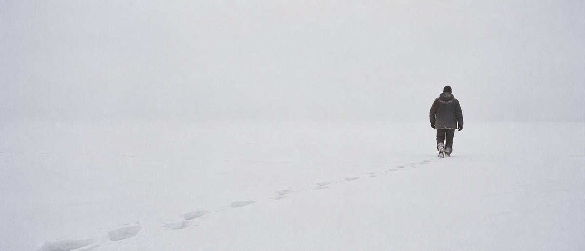 Traces de pas dans un champ de neige blanc, une silhouette au loin