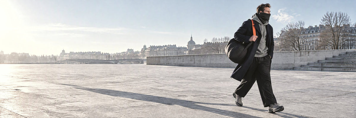 Homme pressé sur une esplanade en hiver, cache-cou noir remonté sur le nez